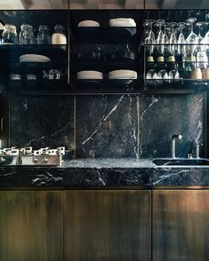 a kitchen with black marble counter tops and gold cabinetry, along with white dishes