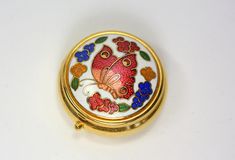 a small round box with flowers and butterflies on it's lid, sitting on a white surface