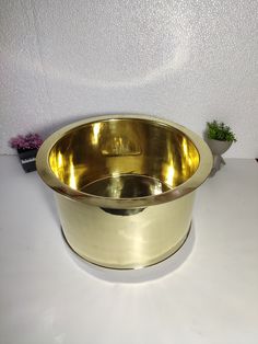 a gold colored bowl sitting on top of a white table next to a potted plant