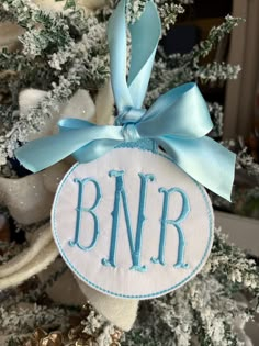 a monogrammed ornament hanging on a christmas tree with blue ribbon and bow