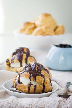 two croissants covered in chocolate drizzle on a white plate next to bowls of pastries