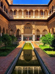 the courtyard of an old spanish style house with water pool in foreground and people walking around