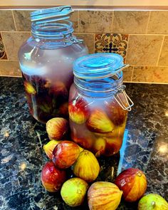 two jars filled with liquid sitting on top of a counter next to some figs