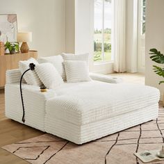 a large white bed sitting on top of a wooden floor next to a plant in a living room