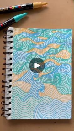 a notebook with an image of the ocean on it and two crayons next to it