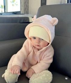 a baby is sitting on the couch wearing a pink bear hat and diaper cover