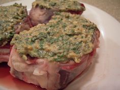 two pieces of meat on a plate with sauce and green stuff around them, sitting on a table