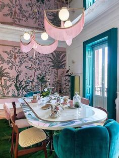 the dining room is decorated with pink and green wallpaper, while blue chairs are set up in front of the table