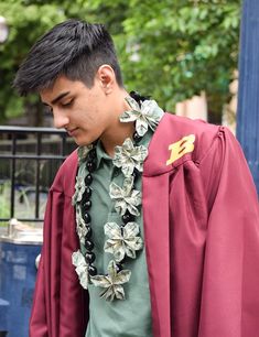 a young man wearing a red graduation robe and flower lei is looking down at his cell phone