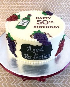 a birthday cake decorated with grapes and a bottle of wine is on a plate that says, happy 50th aged to perfection