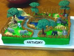 a cake with animals and trees on it sitting on a table next to a bowl