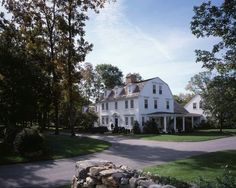 a large white house sitting on the side of a road next to a lush green field