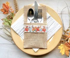 a place setting with silverware and napkins on a plate next to autumn leaves