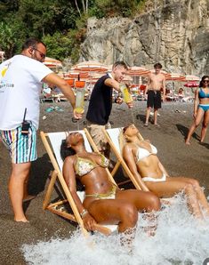 several people on the beach with one woman laying in a chair and two men standing nearby