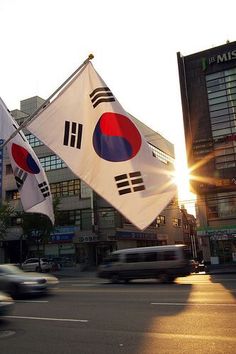 two flags are flying in the air on a city street with buildings and cars behind them