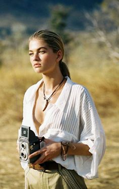 a woman holding a camera in her hand and looking at the camera with no shirt on