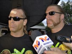 two men in black shirts holding microphones and talking to each other with sunglasses on