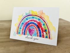 a thank you card with a watercolor rainbow design and a heart on the front