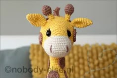 a crocheted giraffe is standing in front of a yellow couch and pillows