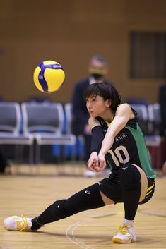 a woman in black and green uniform playing with a yellow volleyball ball on the court