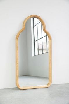 a wooden mirror sitting on top of a cement floor next to a window in a white room