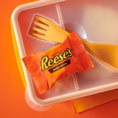 a plastic container with a fork, spoon and orange candy bar wrapper on it