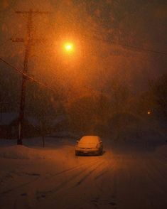 a car driving down a snow covered road at night with street lights in the background