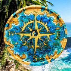 a blue and yellow plate sitting on top of a table next to the ocean with a compass painted on it