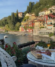 a table with food and drinks on it next to the water in front of some buildings