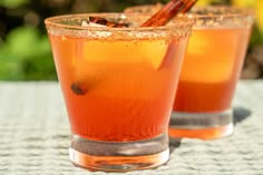 two glasses filled with liquid sitting on top of a table next to each other and cinnamon sticks sticking out of them