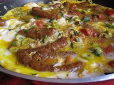 a pizza with sausage, tomatoes and other toppings in a pan on a table