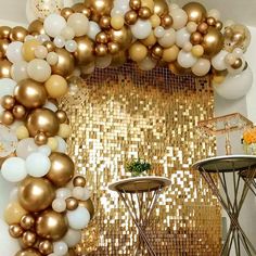 gold and white balloons are hanging from the ceiling in front of a table with chairs