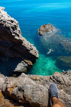 a person standing on top of a rocky cliff next to the ocean with their feet in the water