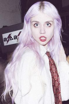 a woman with pink hair wearing a white shirt and tie is posing for the camera