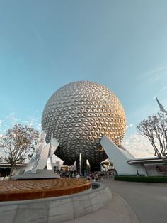 a large ball sitting in the middle of a park next to a building with people walking around it