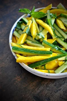 a white bowl filled with cucumbers and green beans on top of a wooden table