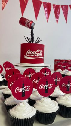 cupcakes with white frosting and coca - cola signs on them are sitting in front of a cake