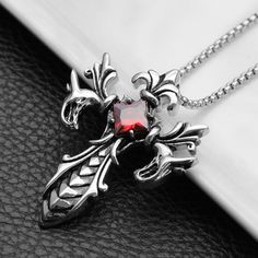 a necklace with a red stone in the center on a black leather surface next to a silver chain