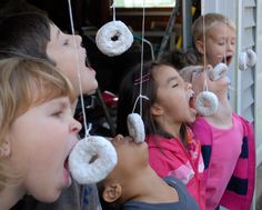 several children with doughnuts hanging from strings in front of their faces and mouths