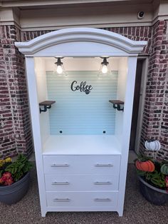 a white cabinet with lights on it and some potted plants in front of it