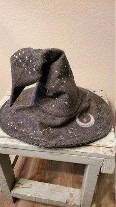 a gray hat sitting on top of a wooden table next to a white chair and wall