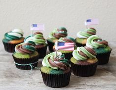 cupcakes with green frosting and an american flag on top are sitting on a table