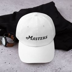 "This Masters hat is simple and classic and ready to be worn at the Masters Golf tournament. This golf hat is an Embroidery that you can wear to watch this Golf tournament at Augusta.  The Masters is coming soon... make sure you get yourself a hat to support one of the greatest golf tournaments in the world. This classic design comes in various colors to match your outfit on Masters sunday! The design is embroidered into the hat/cap. * 100% chino cotton twill * Green Camo color is 35% chino cotton twill, 65% polyester * Unstructured, 6-panel, low-profile * 6 embroidered eyelets * 3 ⅛\" (7.6 cm) crown * Adjustable strap with antique buckle * Blank product sourced from Vietnam or Bangladesh" Masters Hat, Golf Embroidery, The Masters Golf, Masters Golf Tournament, Masters Tournament, Masters Golf, Golf Hat, Golf Tournament, Golf Hats