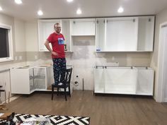 a man standing in the middle of a kitchen with white cabinets and drawers on each side