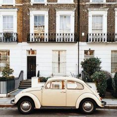 an old car is parked in front of a row of white brick buildings with balconies