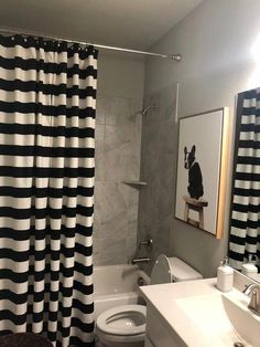 a white toilet sitting next to a bath tub in a bathroom under a mirror with black and white striped curtains