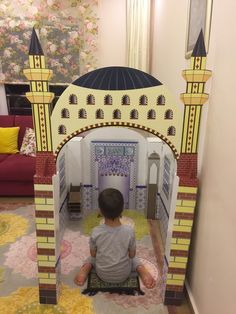 a little boy sitting on the floor in front of a fake building with a dome