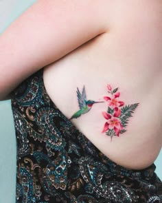 a woman's stomach with pink flowers and a hummingbird tattoo on her left side