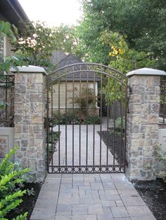 an iron gate in front of a brick house with trees and bushes around it,