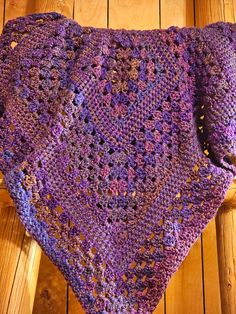 a purple crocheted blanket sitting on top of a wooden floor